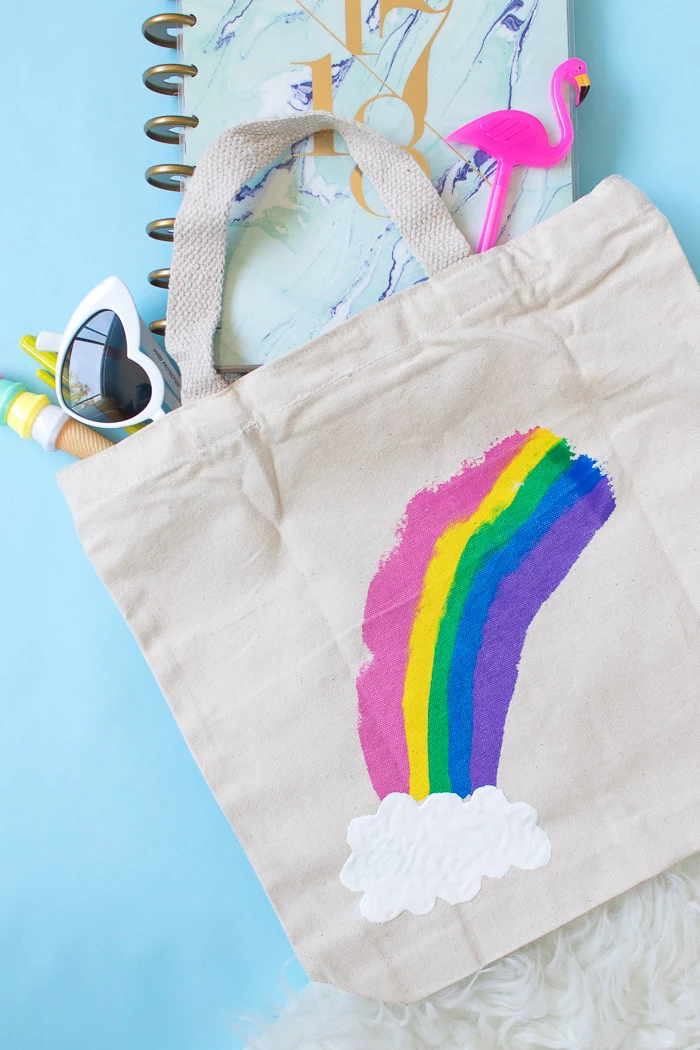 creative homemade gifts, tote bag with rainbow and cloud painted on it, placed on blue surface with notebook