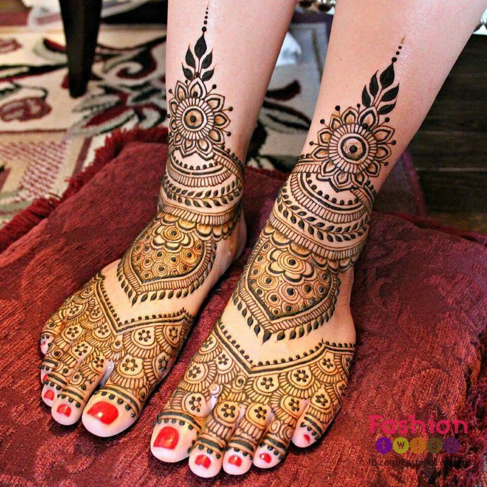 identical floral designs, on a pair of feet, with red nail polish, henna foot tattoo, dark brown with many symmetrical details 