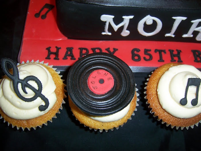 musical note in black, miniature vinyl record, and a treble clef, all made from fondant, topping three cupcakes, with white frosting