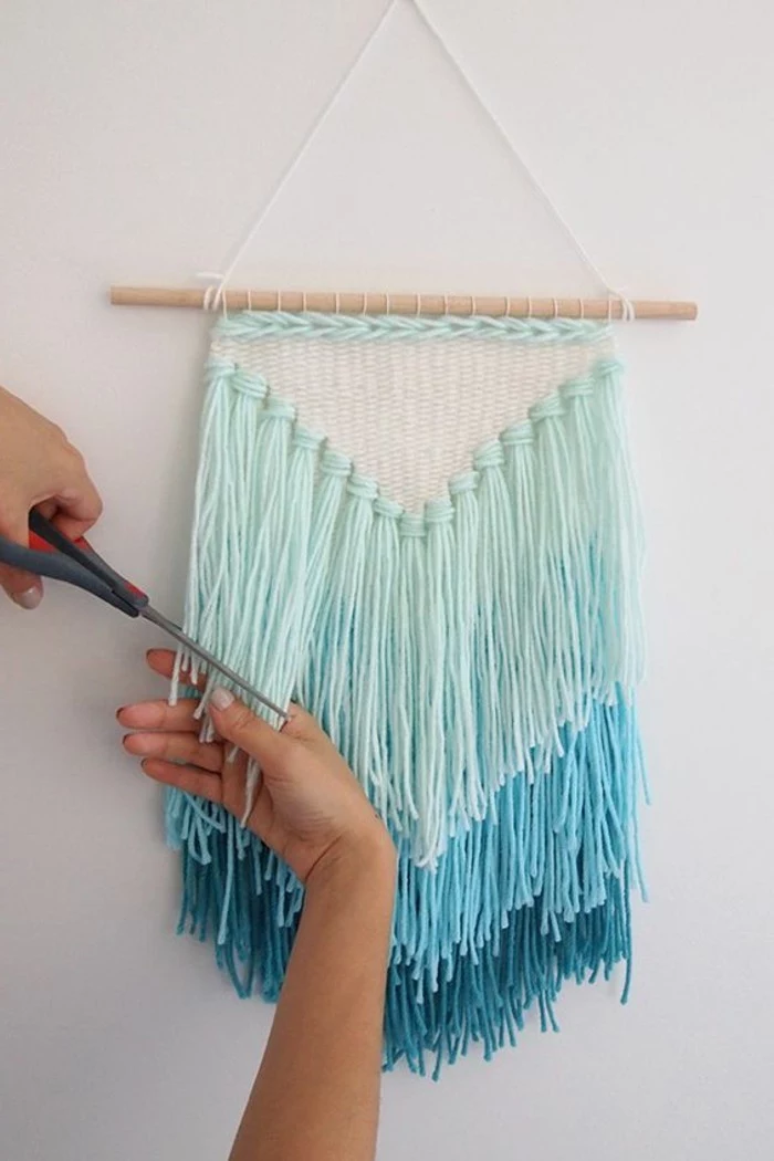 scissors held by a hand, trimming the tassels of a wall decoration, inspired by a dream catcher, in three shades of turquoise