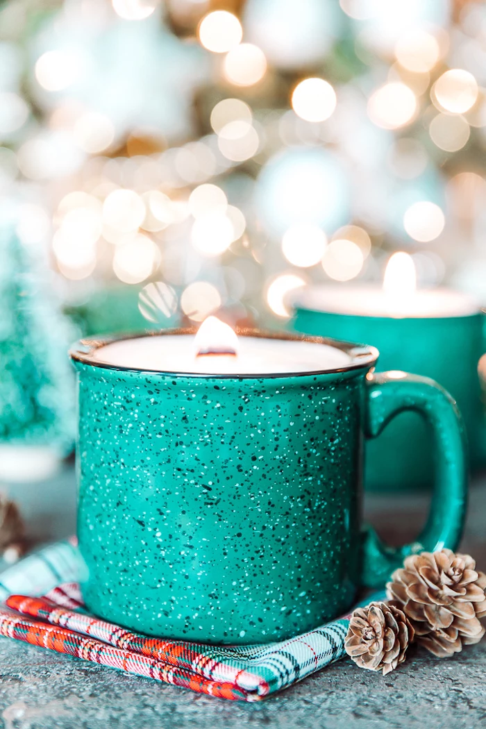 turquoise metal mug, candle inside, placed on a table cloth, homemade christmas gift ideas, pine cones on the side