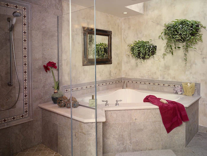 corner bathtub in white and grey, inside a room, containing a shower, two potted plants, a mirror and a red towel