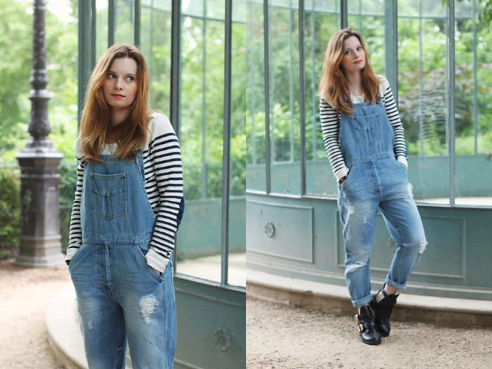 ginger-haired young woman, wearing vintage denim overalls, and a striped white and black jumper, standing with hands in her pockets