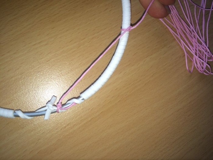 pink thread tied to a wire hoop, wrapped with a white leather rope, how to weave a dreamcatcher, on a light wooden surface