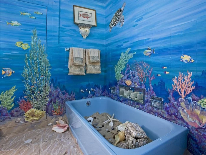 tropical fish and water turtles, seaweed and different kinds of corals, painted on the walls of a room, modern bathroom ideas, blue bathtub filled with sand, seashells and starfish