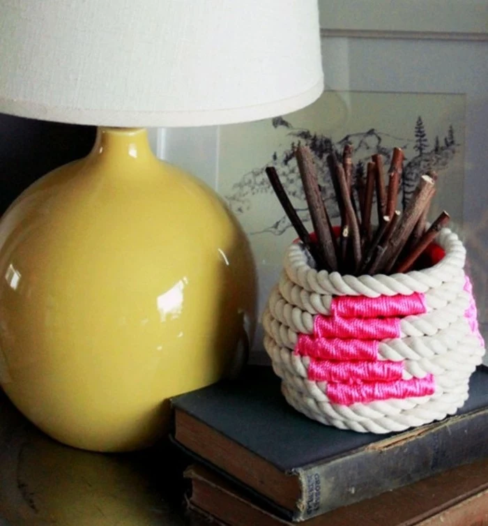 rope in off-white, decorated with hot pink thread, and wrapped around a small vase, containing shirt dried twigs, yellow lamp nearby