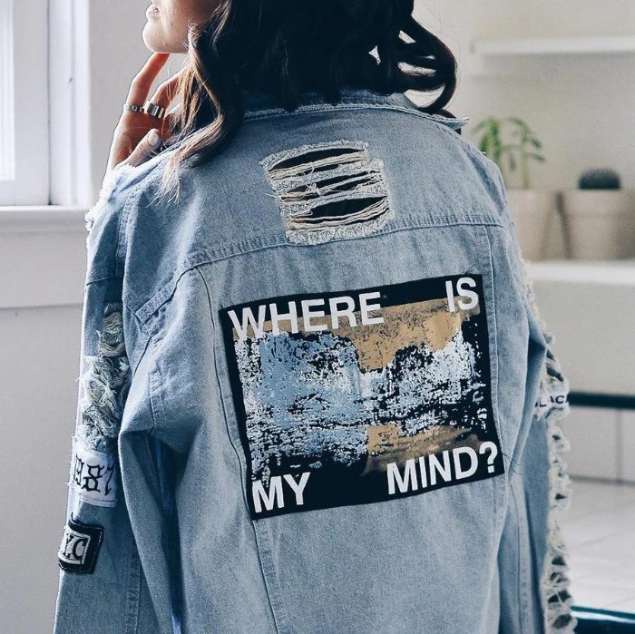 statement denim jacket, with rips and faded patches, worn by brunette woman, with her face turned away, where is my mind, written with white letters 
