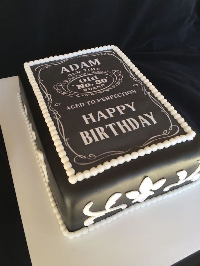 rectangular party cake, covered in smooth black fondant, and decorated with white frosting, made to look like a whiskey label, with the inscription happy 60th birthday