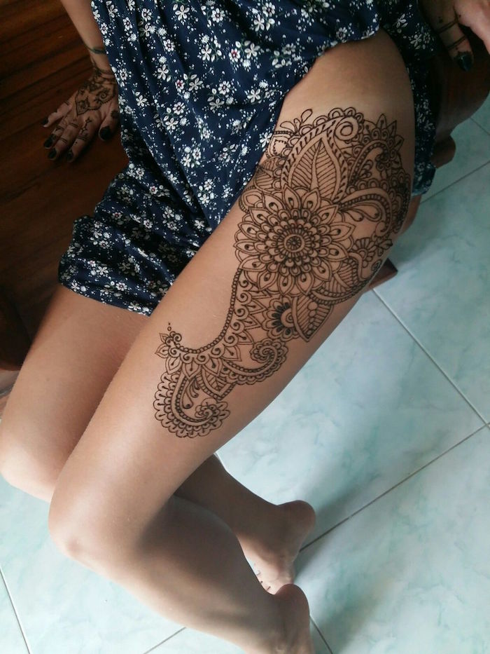thigh temporary tattoo, featuring a mandala and lots of details, cute henna, worn by a woman, in a dark blue dress, with white floral pattern