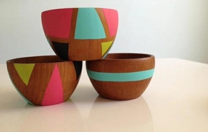 three wooden bowls, decorated with geometric shapes, in turquoise and neon pink, yellow and black, homemade gift ideas, stacked on a white surface