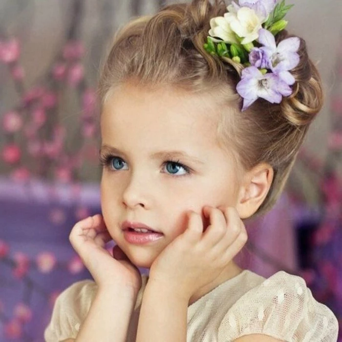 crocus-like flowers, in pale yellow and violet, decorating the dark blonde up-do, of a young, blue-eyed child, in a cream formal dress