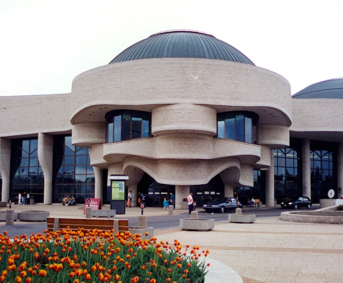 museum of civilization in canada, pale beige building, with round and wave-like elements, lots of glass panels, and grey domes, modernism and postmodernism, tulip garden nearby