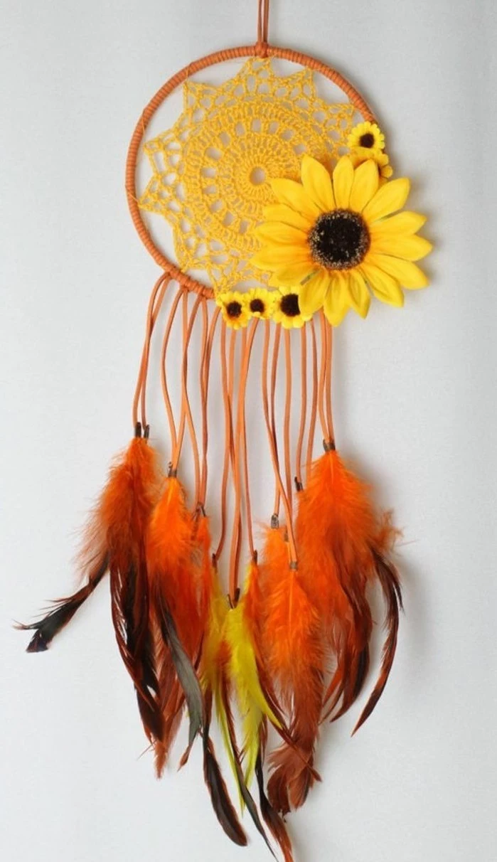 sunflower ornaments in different sizes, on an orange dreamcatcher, with a yellow crochet doily, and orange and yellow feathers, dreamcatcher designs, hanging on a white wall
