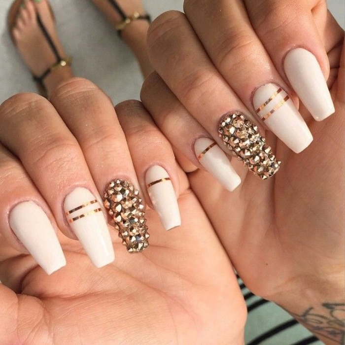 nude gel nails, with long coffin shape, in off-white, decorated with 3D, gold nail decall stickers, and metallic gold stripes