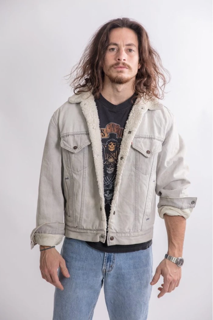 bearded man with a mustache, and shoulder length wavy hair, wearing 80s clothes, pale retro jeans, black rock band t-shirt, pale denim jacket with flannel trim, typical 80s fashion