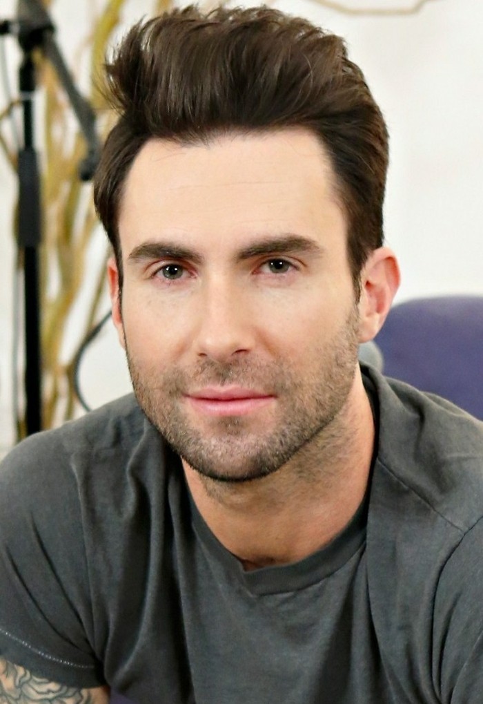 maroon 5 frontman, adam levine, with a short sides long top haircut, and stubble on his jaw, dark brunette hair styled in a quiff