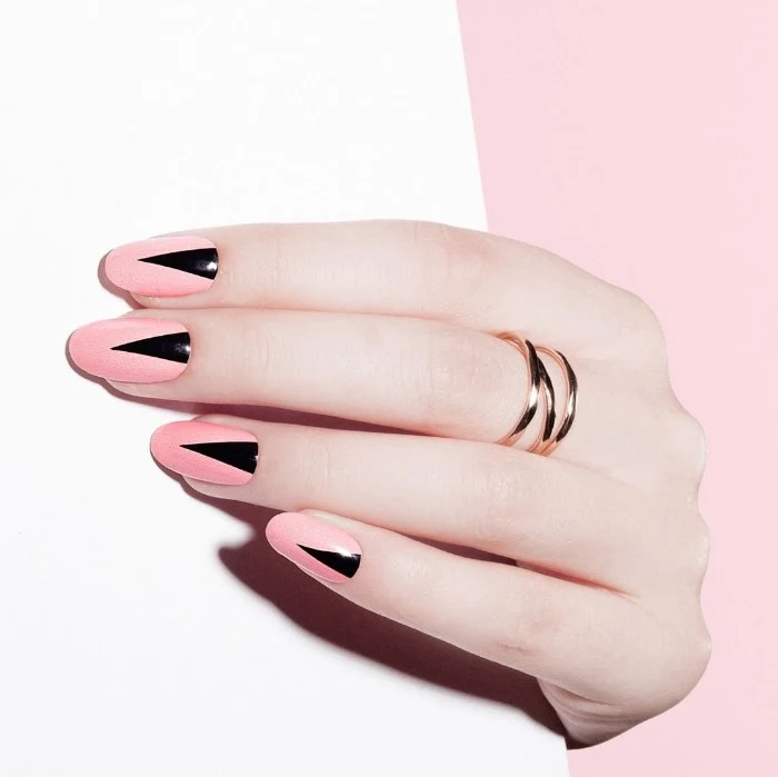 candy pink manicure, decorated with black triangles, on a pale hand, wearing a golden ring, almond shaped nails