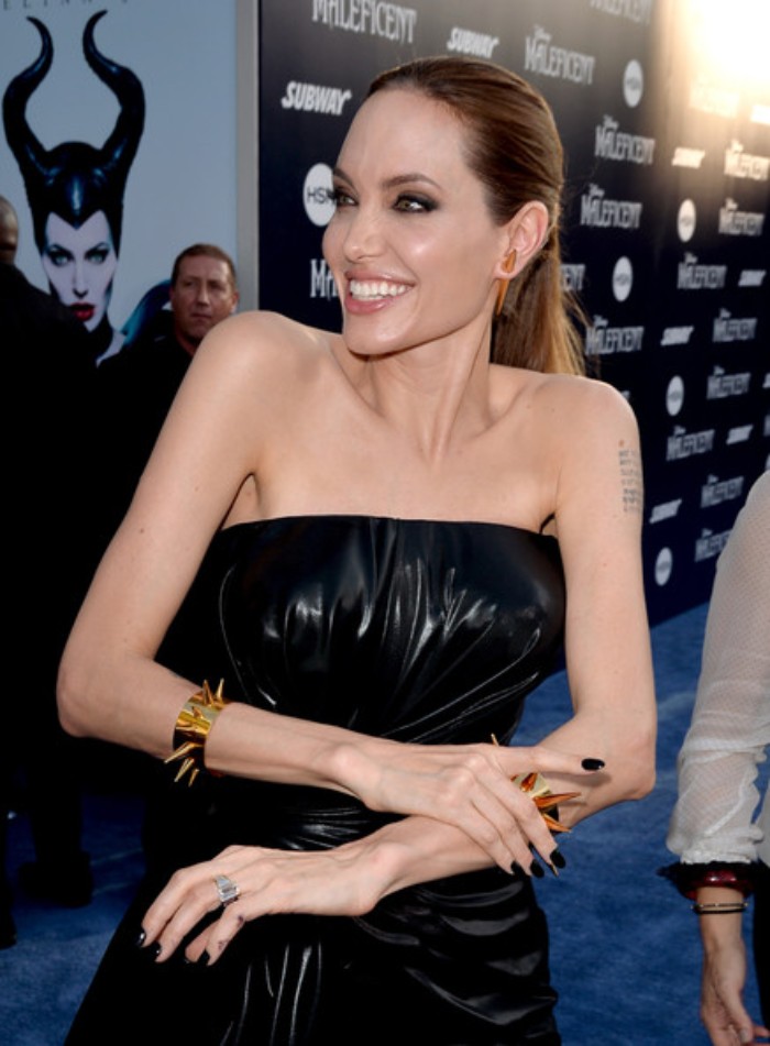 jet black short stiletto nails, worn by angelina jolie, smiling and dressed in a black, glossy sleeveless dress