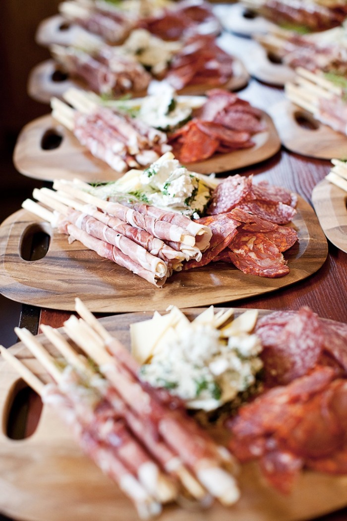 horderves, wooden platters with a selection of salami, cheeses and bread sticks with prosciutto, placed on a table