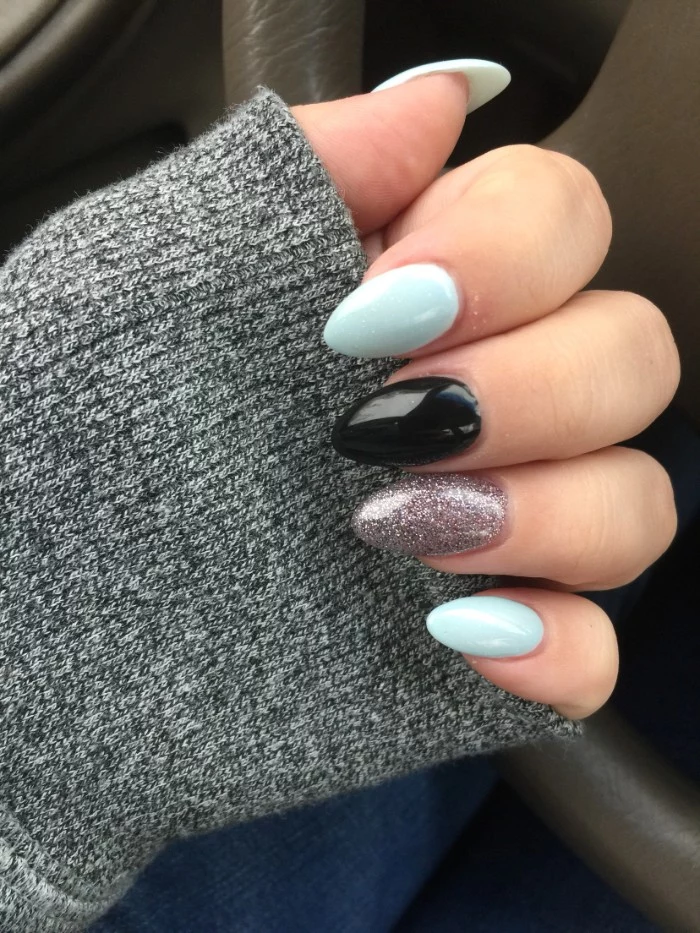 short stiletto nails, in pale blue, black and silver glitter, worn by a pale hand, dressed in a grey sleeve
