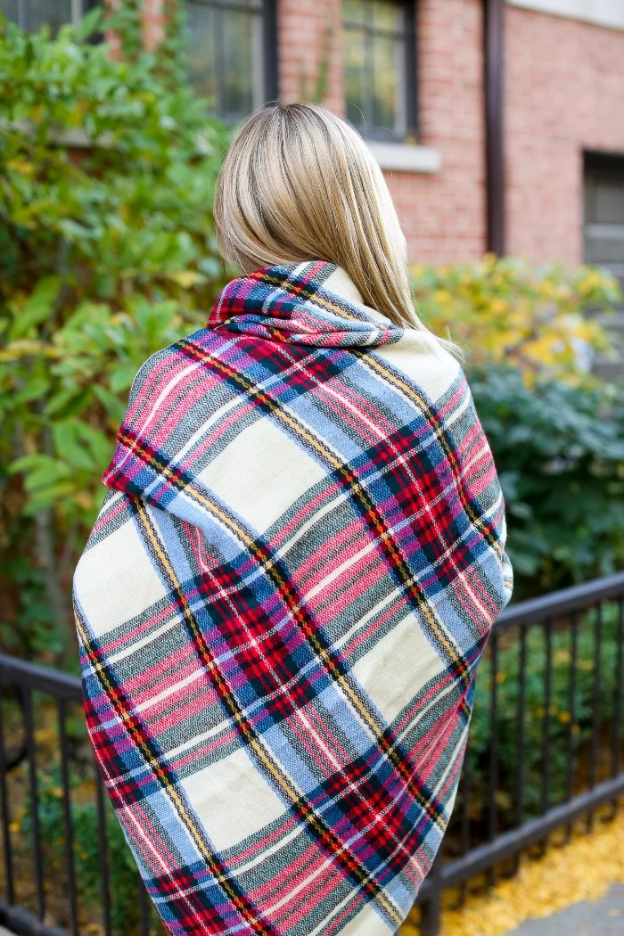 view from the back, showing a blonde woman, wrapped in a large white and red, black and blue tartan scarf, how to wear a blanket scarf, around the shoulders