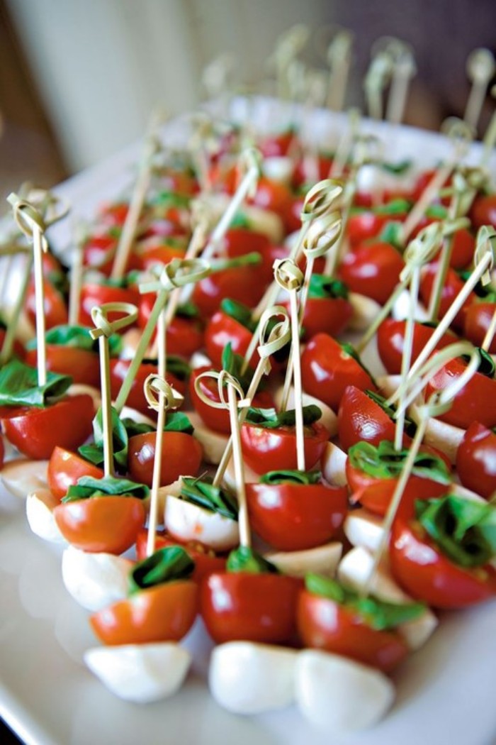 many small skewers, with mozzarella and cherry tomatoes, and fresh basil leaves, served on a large white plate