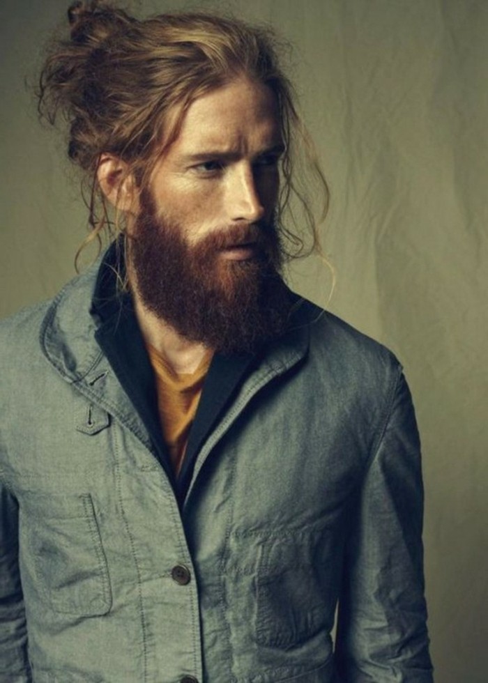 man with long beard, and wavy long brunette hair, tied in a messy bun, short haircuts for men, loose strands of hair near his forehead