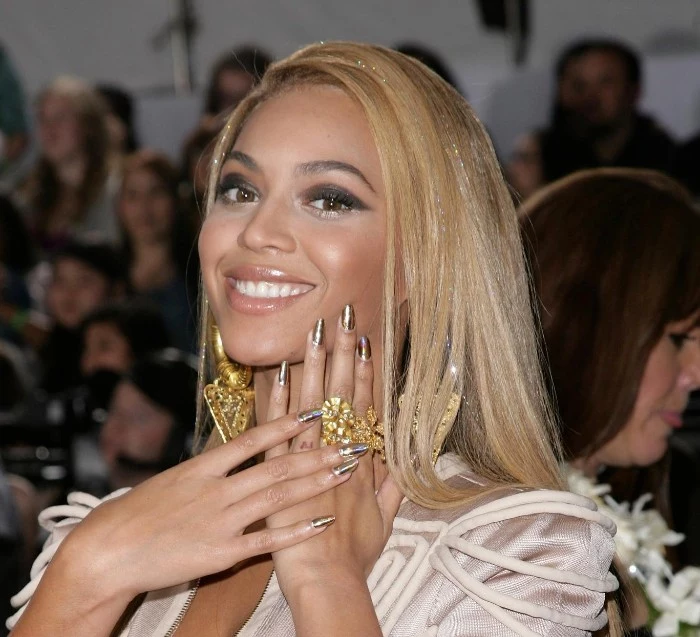 smiling beyonce with smooth blonde hair, bold dark eye make up, and almond shaped nails, painted in a silver shade