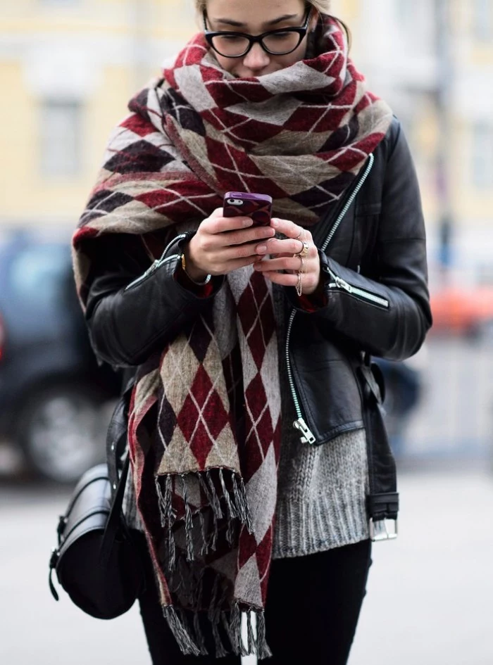 bulky patterned scarf, worn around the neck of a young girl, in a black leather biker jacket, black trousers and a pale grey knitted sweater, scarf outfits for every day wear