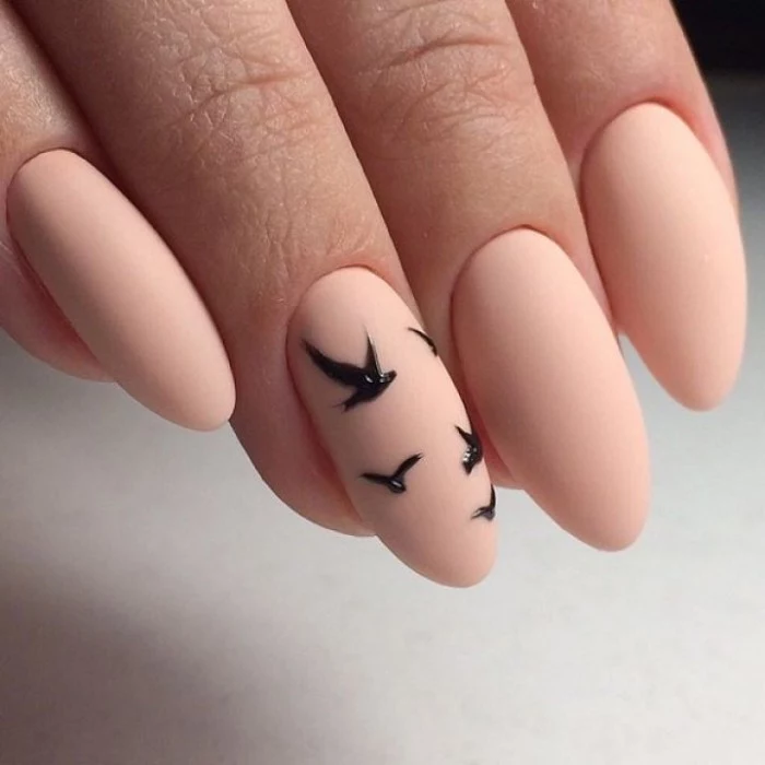 tiny bird-shaped motifs in black, on nude peach pink matte stiletto nails, seen in extreme close up