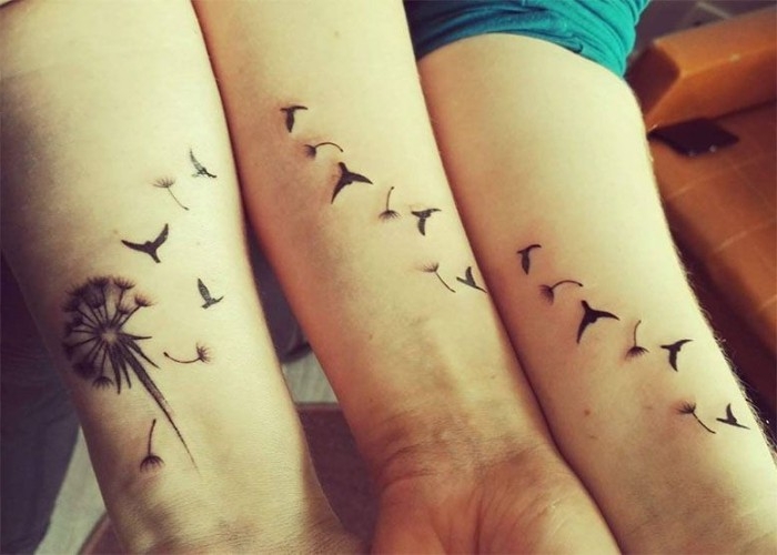 dandelion seeds and birds in flight, tattooed in black ink, accross three arms, matching friend tattoos, one arm has a half-blown dandelion flower