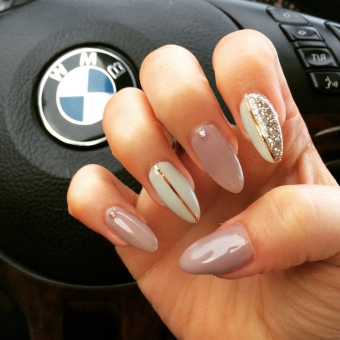 steering wheel of a bmw, behind a hand with folded fingers, and long and pointy, ash pink nude gel nails, decorated with white, silver glitter and metallic gold motifs