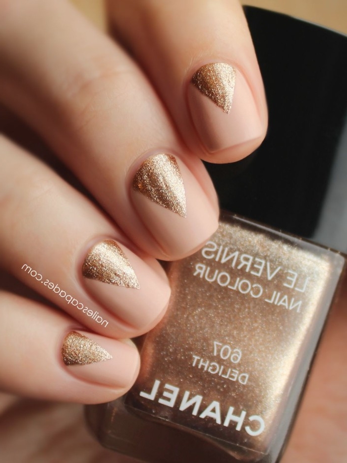 triangles painted in sparkly rose gold, on top of four nails, with nude pink nail polish, on a hand, holding a bottle of rose gold nail polish