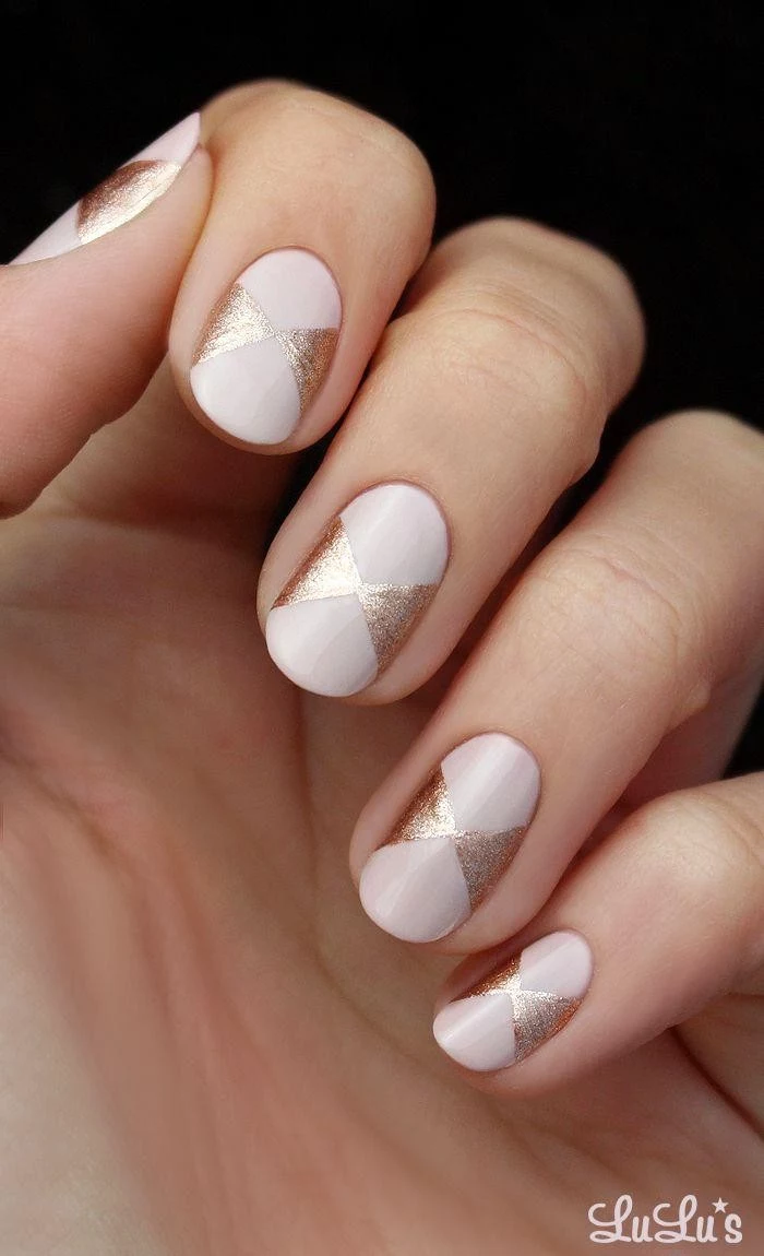 milky pink nude nails, decorated with bow-like motifs, drawn in sparkly rose gold, on a pale hand with folded fingers