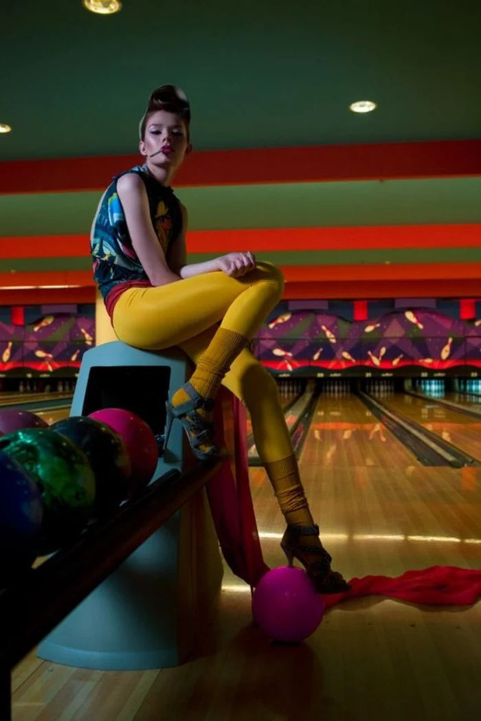yellow leggings and matching yellow leg warmers, worn with teal high heeled sandals, 80s outfits, by a young woman in a bowling alley