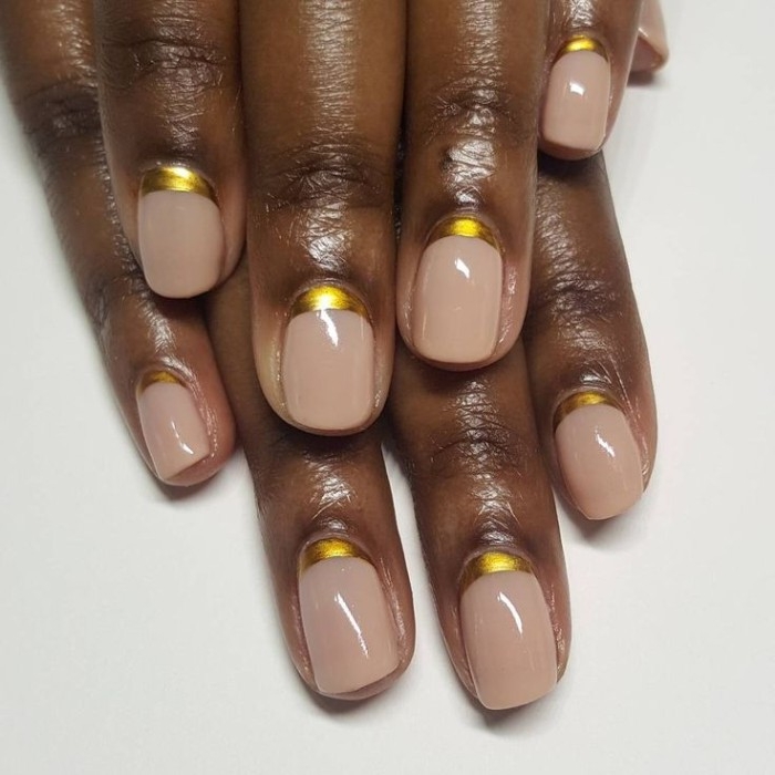 gold metallic details, at the base of nude nails, attached to two dark brown hands, one placed on top of the other