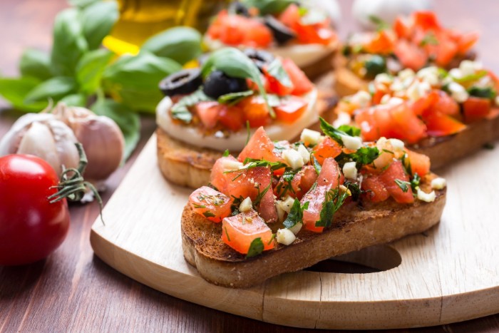 classic bruschetta with chopped tomato, mozzarella and paisley, garlic and olives, hor dourves on a wooden board