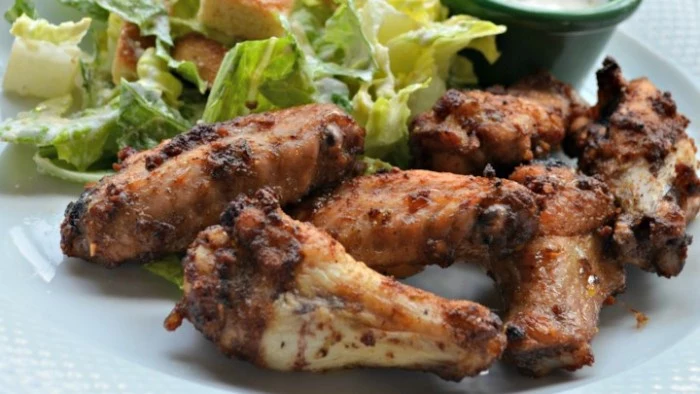 buffalo wings seen in close up, hour derves, next to a side of green salad, and a small dish with dip