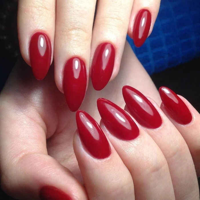 deep red glossy nail polish, on almond shaped nails, worn by two pale hands, seen in close up