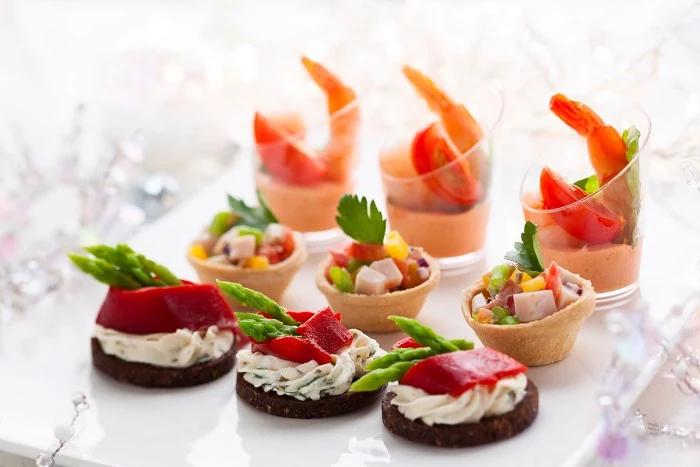 nine colorful hors dourves, prawn cocktails in small glasses, tiny edible baskets with veggies, crackers with creamy spread, peppers and asparagus