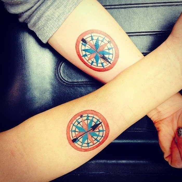 round tattoos in red and white, with blue and black details, depicting two matching compasses, husband and wife tattoos, on the lower part, of two crossed arms