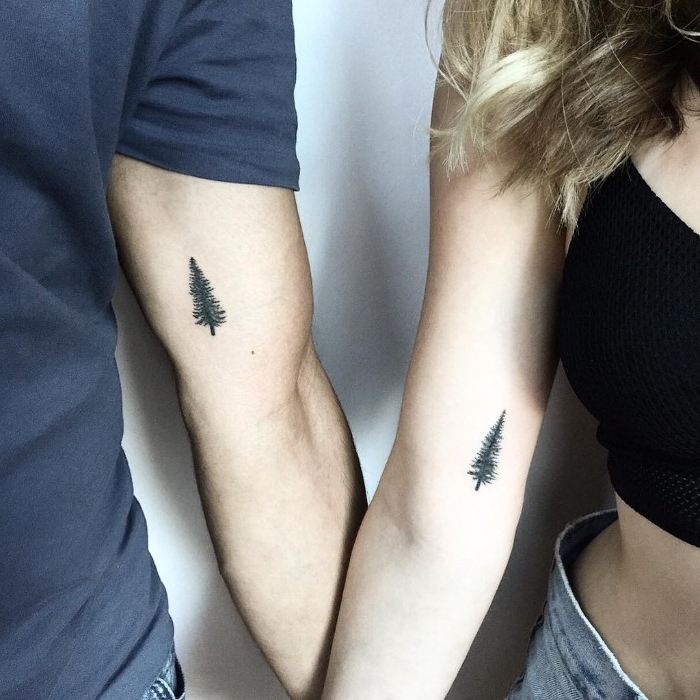 fir tree tattoos, done in black, above the elbows of two linked arms, his and hers tattoos, matching identical design