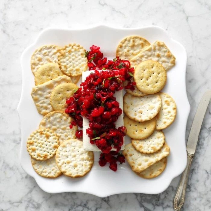 cranberry confit and brie chiese, on a white ceramic plate, containing various kinds of crackers, appetizers for a crowd, for christmas or thanksgiving