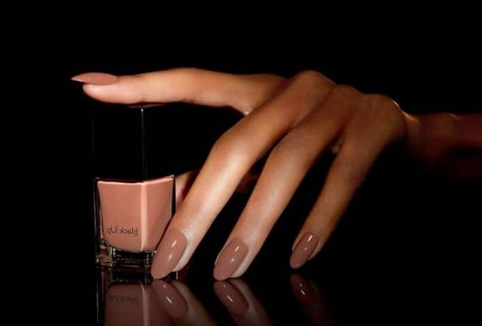 mocha-colored nail polish, on a hand with long, slender fingers and oval nails, with a nail polish bottle