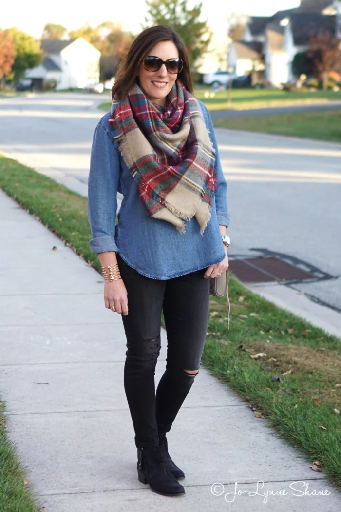 sunglasses worn by a brunette woman, in a denim shirt, and ripped black skinny trousers, with a beige plaid scarf around her neck