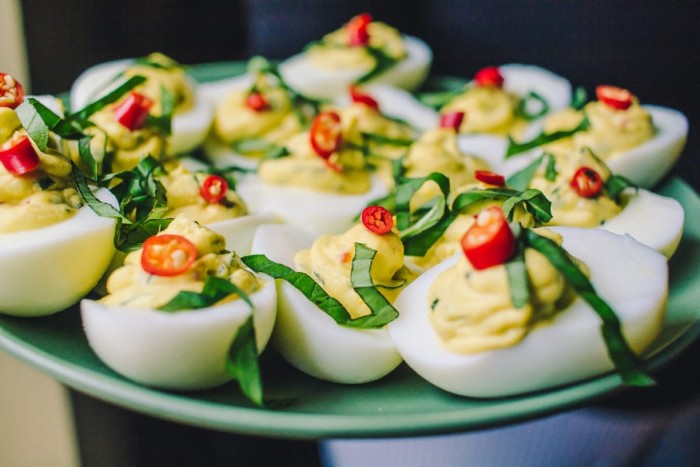 hor d oeuvres, pale blue plate, containing devlled eggs, topped with chopped fresh basil, and red chili slices