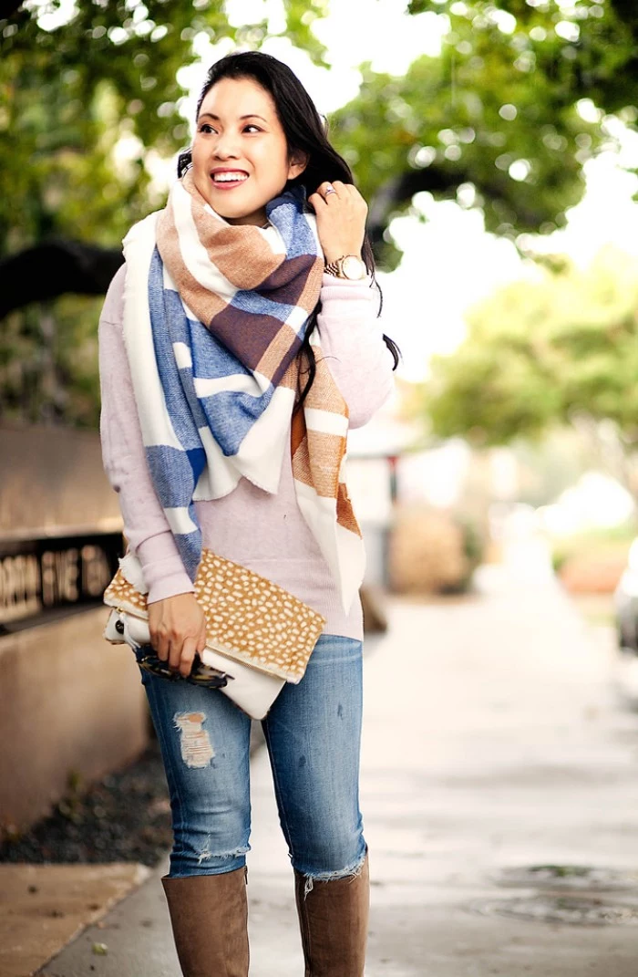 ripped blue jeans, worn with an off-white jumper, and a bulky blanket shawl, by a smiling east asian woman, holding a clutch bag