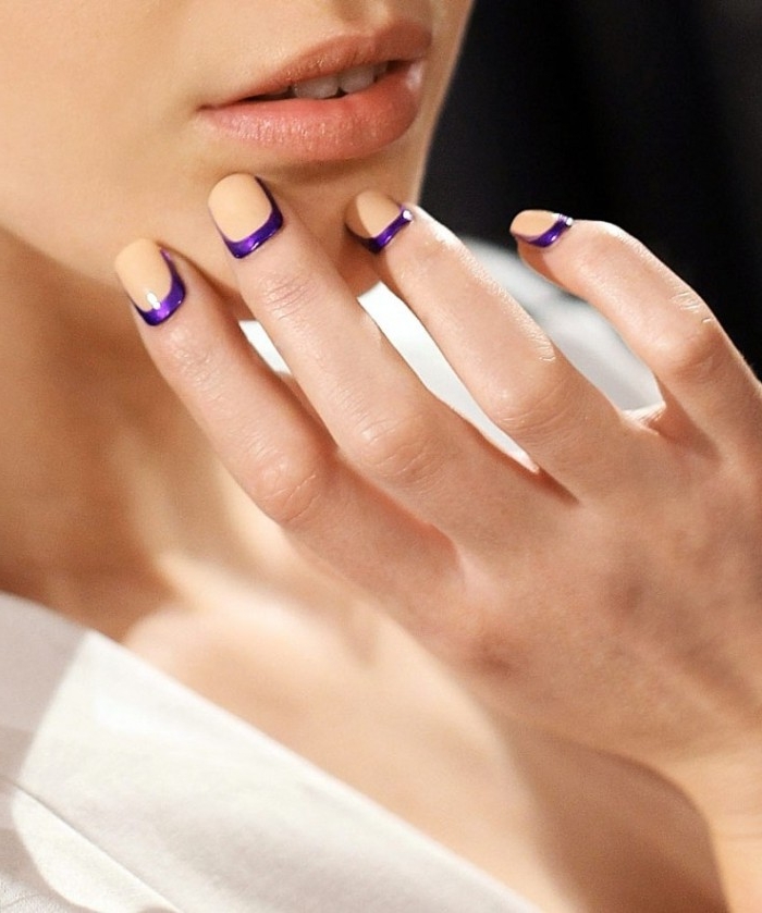 young woman in a white shirt, holding a hand to her face, square manicure with nude nail polish, and dark violet elements