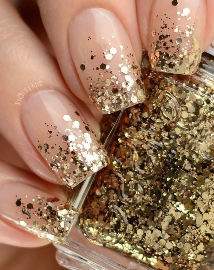 flakes of gold glitter, decorating the tips of four square nails, nude nails with glitter, on a hand holding a bottle, of gold glitter nail polish