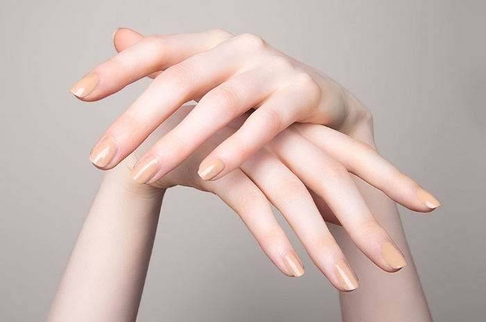 peach colored nude nail polish, on the short, square nails of two very pale hands